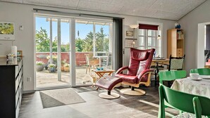 Una habitación amplia con un portón corredizo de vidrio que da a un patio exterior, un sillón de cuero rojo, una silla verde y una pequeña mesa con una taza.