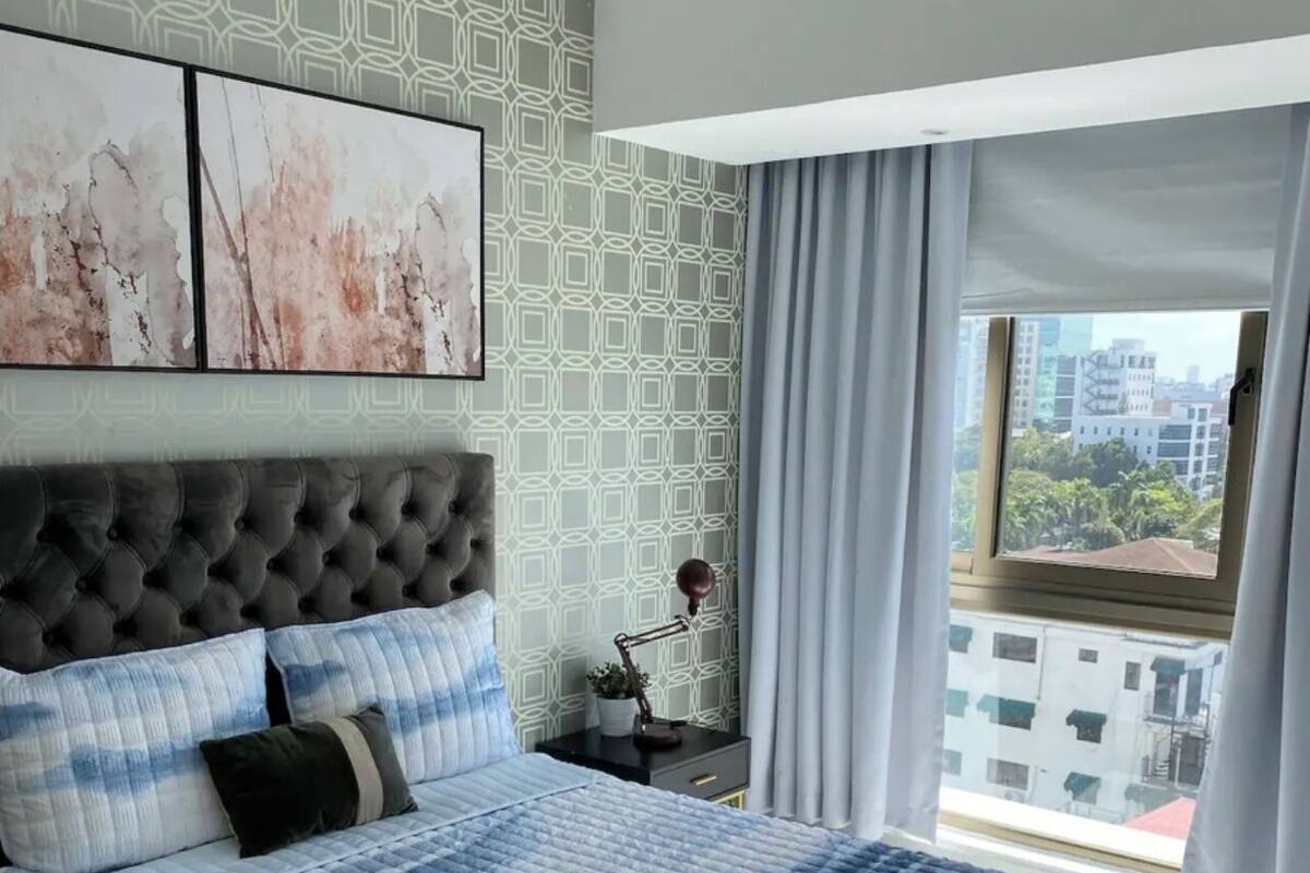 A bedroom with a large bed, a tufted headboard, and a city view through a window.