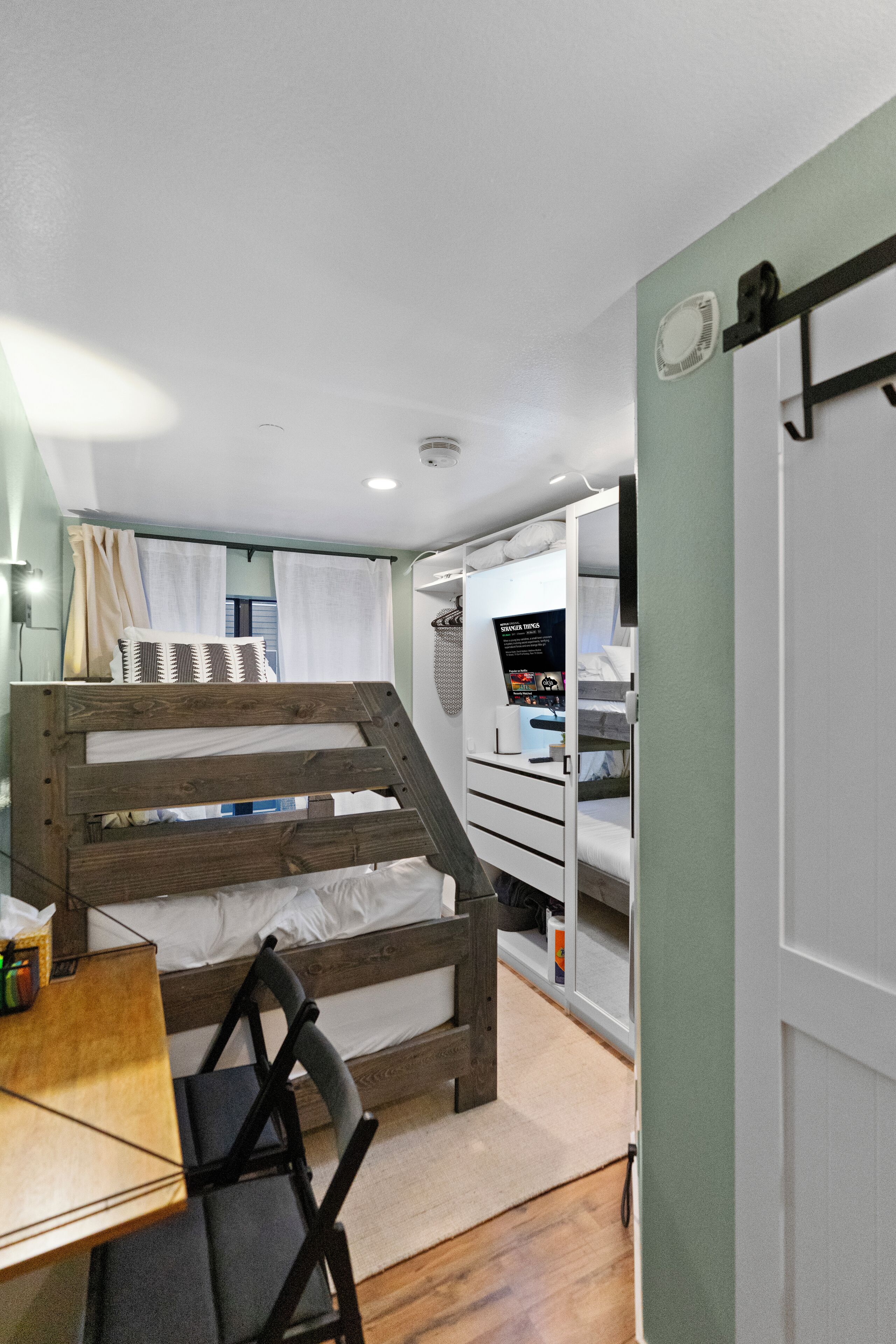Una habitación pequeña con una cama litera, un escritorio con silla y una mesita.