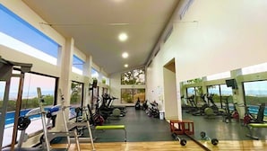 A spacious gym with wooden flooring, various exercise equipment, large windows, and a view of the outdoors.