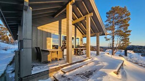 A covered outdoor area with a table and chairs, surrounded by snow, overlooking a snowy landscape with trees.