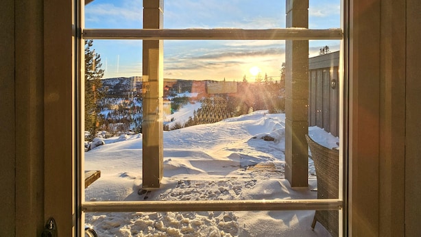 A view through a window of a snowy landscape with a wooden structure and a clear sky.