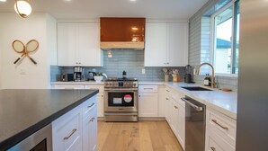 Une cuisine moderne avec des meubles blancs, une cuisinière en acier inoxydable et une grande fenêtre qui laisse entrer la lumière naturelle.