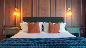 Un lit bien fait, recouvert d’une couverture bleue, avec deux oreillers marron et une tête de lit verte. Deux lampes de chevet sont placées de chaque côté du lit.