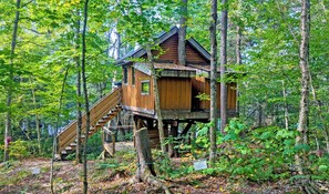 Een houten boomhuis met een trap, omringd door dicht bos.