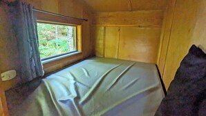 Une petite cabine avec un lit simple et une fenêtre donnant sur une forêt.