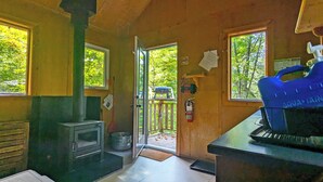 L’intérieur d’un chalet rustique comprend un coin cuisine, un distributeur d’eau bleue et une porte donnant sur une terrasse avec vue sur les arbres.