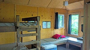 Une cabine avec des lits superposés, une fenêtre avec des rideaux, une carte accrochée au mur et un banc avec un coussin.
