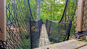 A rope bridge in a forested area with a picnic table and benches in the background.