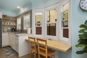 Une cuisine avec des meubles blancs, une table à manger en bois et une horloge au mur.