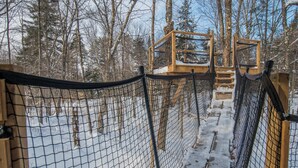 Une forêt enneigée avec une plateforme d’observation en bois et des barrières de sécurité en filet.