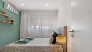 Un dormitori amb llit, una tauleta de nit, una làmpada, una finestra amb cortines i aire condicionat.