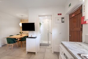 A hotel room with a dining area, a TV, a shower, and a wooden door.