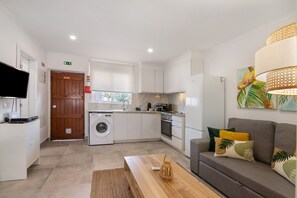 A modern kitchen with white cabinets, a washing machine, and a dining area with a wooden table and sofa.