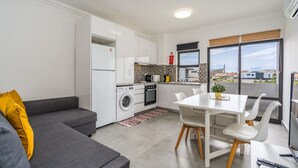 Un appartement moderne avec un canapé gris, une table à manger avec des chaises, une cuisine équipée et une grande fenêtre.