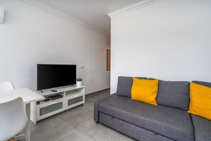 Un salon moderne avec un canapé gris, un téléviseur à écran plat posé sur un meuble blanc et un bureau blanc.