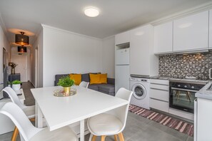 Une cuisine moderne avec des meubles blancs, une table à manger avec des chaises, un lave-linge et un four encastré.