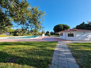Una piscina, un edificio blanco con techo de tejas y un sendero pavimentado.