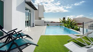 A modern outdoor pool area with lounge chairs, a clear blue sky, and a view of the city. - Holiday Home 'Pico Do Paraíso' with Sea View, Wi-Fi and Air Conditioning (Funchal)