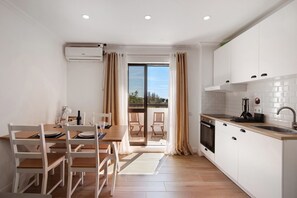 A modern kitchen with white cabinets, a dining area with wooden chairs, a large sliding glass door to a balcony, and a built-in oven. - Apartment 'Lovely and New  In Oura' with Private Pool, Wi-Fi and Air Conditioning (Albufeira)