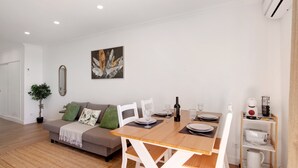 A modern living room with a sofa, dining table, chairs, a coffee machine, and a plant.