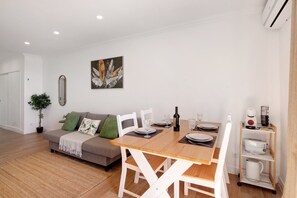 Un salon moderne comprenant un canapé, une table à manger, des chaises, une machine à café et une plante.