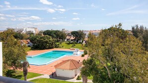 A swimming pool with a tiled deck, surrounded by greenery and buildings in the background.