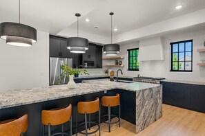 A modern kitchen with a marble island, black cabinets, and pendant lighting. - Our Place; Our Home has an inside slide, gourmet kitchen, view for days, and just feels like home! (Hurricane)