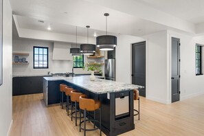 A modern kitchen with a marble island, bar stools, pendant lights, and a refrigerator. - Our Place; Our Home has an inside slide, gourmet kitchen, view for days, and just feels like home! (Hurricane)