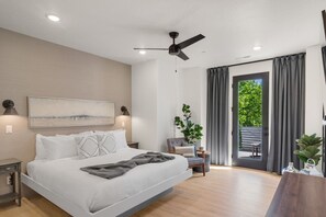 Ein modernes Schlafzimmer mit einem großen Bett, Deckenventilator, einer Schiebeglasdoor zum Balkon und Blick ins Grüne.