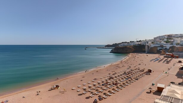 A beach with rows of sun loungers and umbrellas, a clear sky, and buildings in the background. - Apartment 'City Center' with Balcony, Wi-Fi and Air Conditioning (Albufeira)
