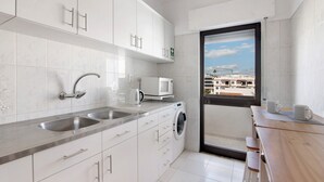 A modern kitchen with white cabinets, a built-in washing machine, and a view through a glass door. - Apartment 'City Center' with Balcony, Wi-Fi and Air Conditioning (Albufeira)