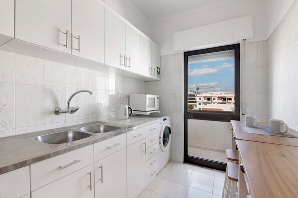 A modern kitchen with white cabinets, a built-in washing machine, and a view through a glass door.