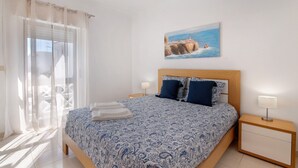 A bedroom with a bed, a nightstand, a painting, and a view of the sea. - Apartment 'City Center' with Balcony, Wi-Fi and Air Conditioning (Albufeira)