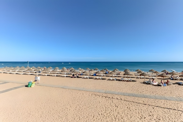 A beach with sun loungers and umbrellas, a clear sky, and the ocean in the background.