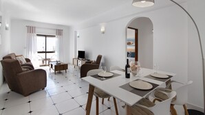 A modern living room with a sofa, dining table, and chairs, a TV, and a large window with curtains. - Apartment 'City Center' with Balcony, Wi-Fi and Air Conditioning (Albufeira)