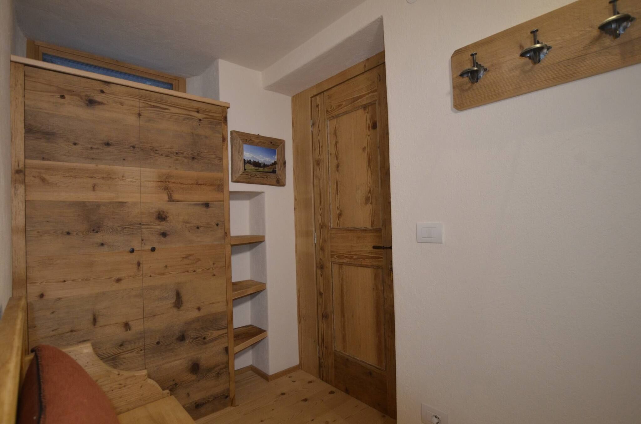 Une armoire en bois avec des étagères, une porte en bois et un porte-manteau fixé au mur.