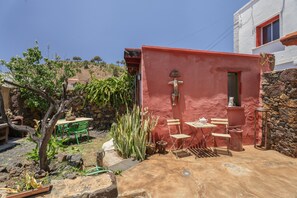 A red-walled outdoor area with a table and chairs, a small tree, and a stone wall.