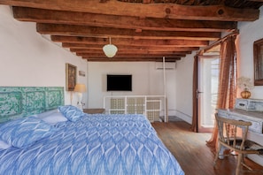 A bedroom with a bed, wooden ceiling beams, a TV, and a desk with a chair.