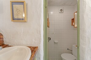 A bathroom with a wooden vanity, a framed picture on the wall, a white toilet, and a shower area.