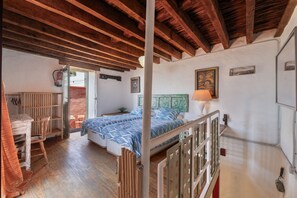 A bedroom with a wooden ceiling, a bed with a blue and white patterned bedspread, a bedside table, and a window with a view.