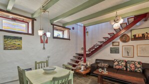 Un área de comedor con una mesa y sillas de madera, una escalera con barandillas rojas y un sofá con cojines estampados.