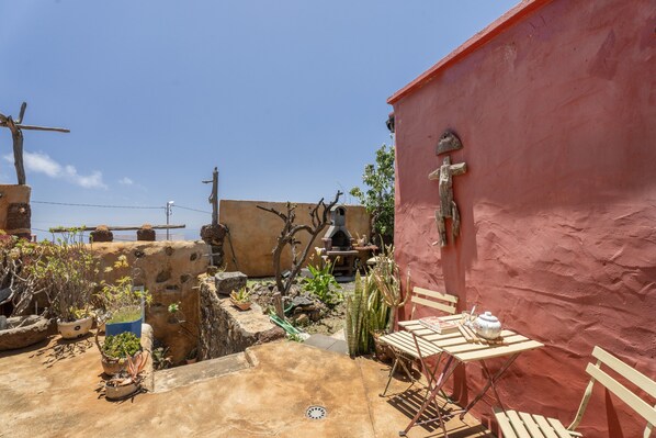 A red building with a small patio area featuring a table and chairs, potted plants, and a rustic outdoor setting.