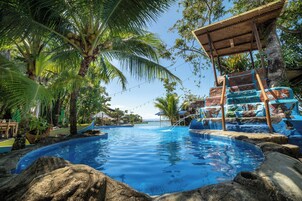 Un resort tropical con una piscina azul cristalina, palmeras y una estructura de madera con un letrero que dice 'Jacuzi'.