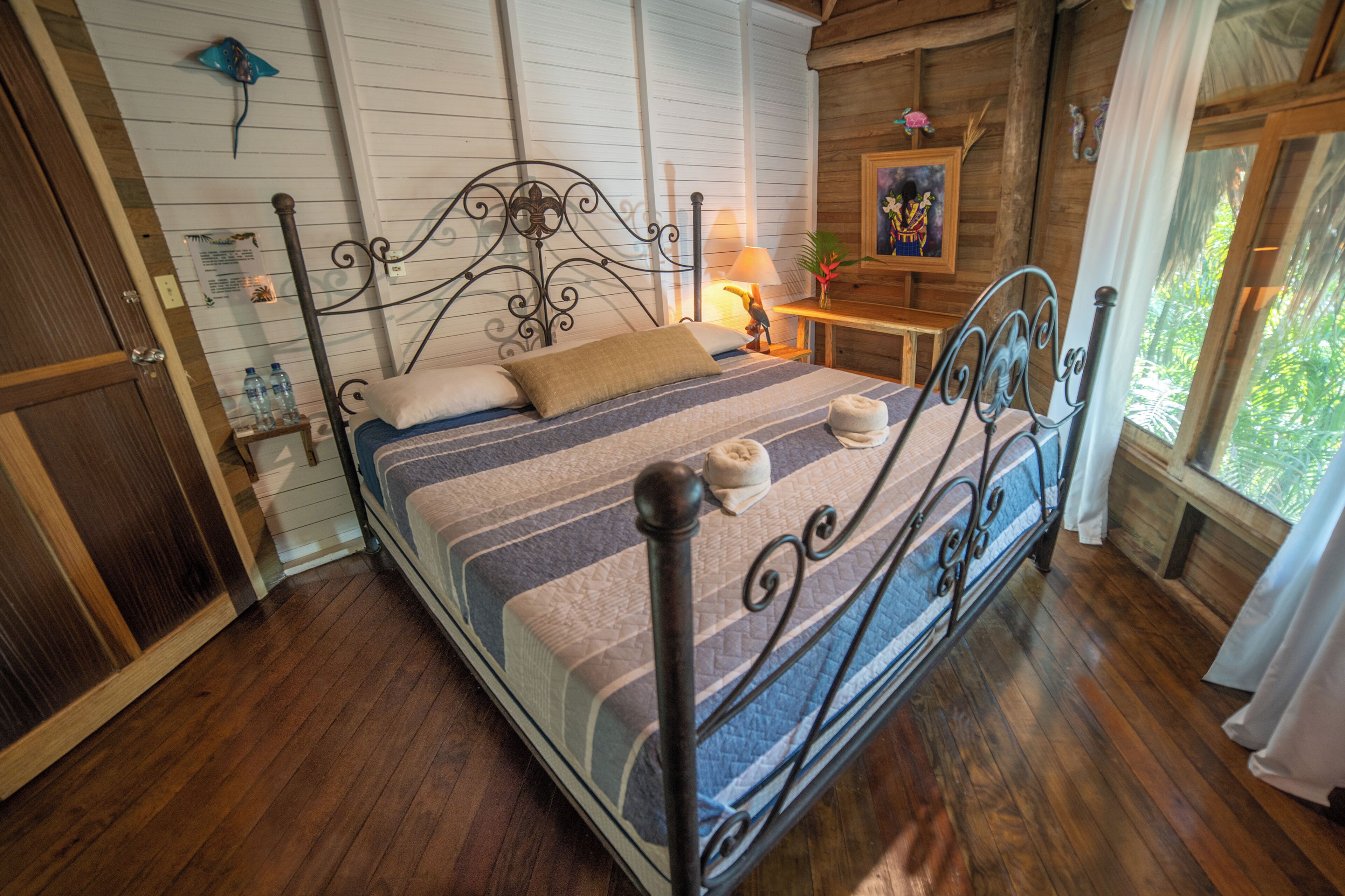 A wooden-framed bed with a metal headboard, a bedside table with a lamp, and a window with curtains.