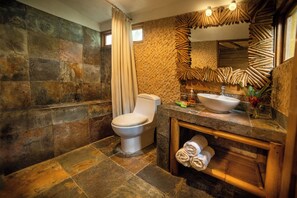 Une salle de bain avec un mur en pierre, des toilettes, un lavabo et un miroir au design original.