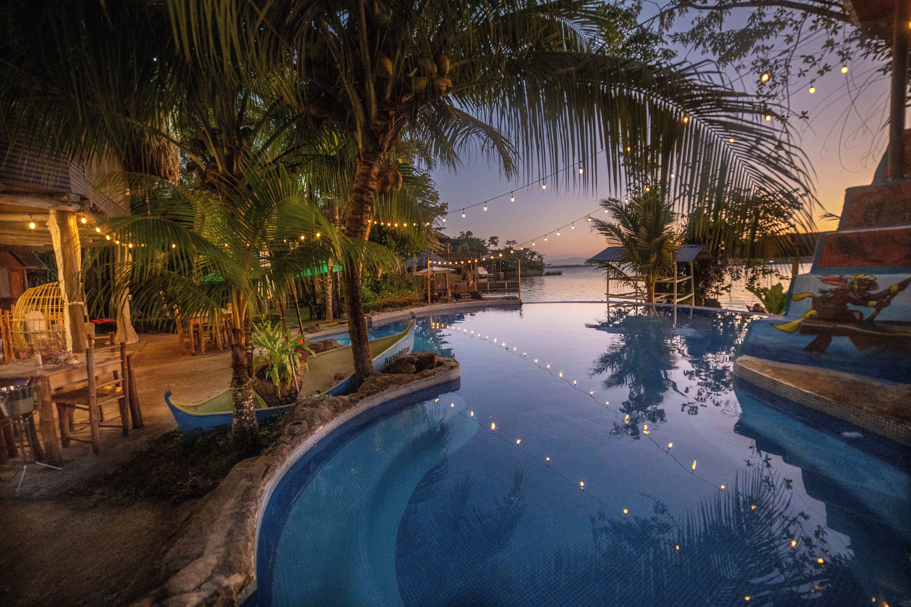 A swimming pool with a boat, palm trees, and string lights.
