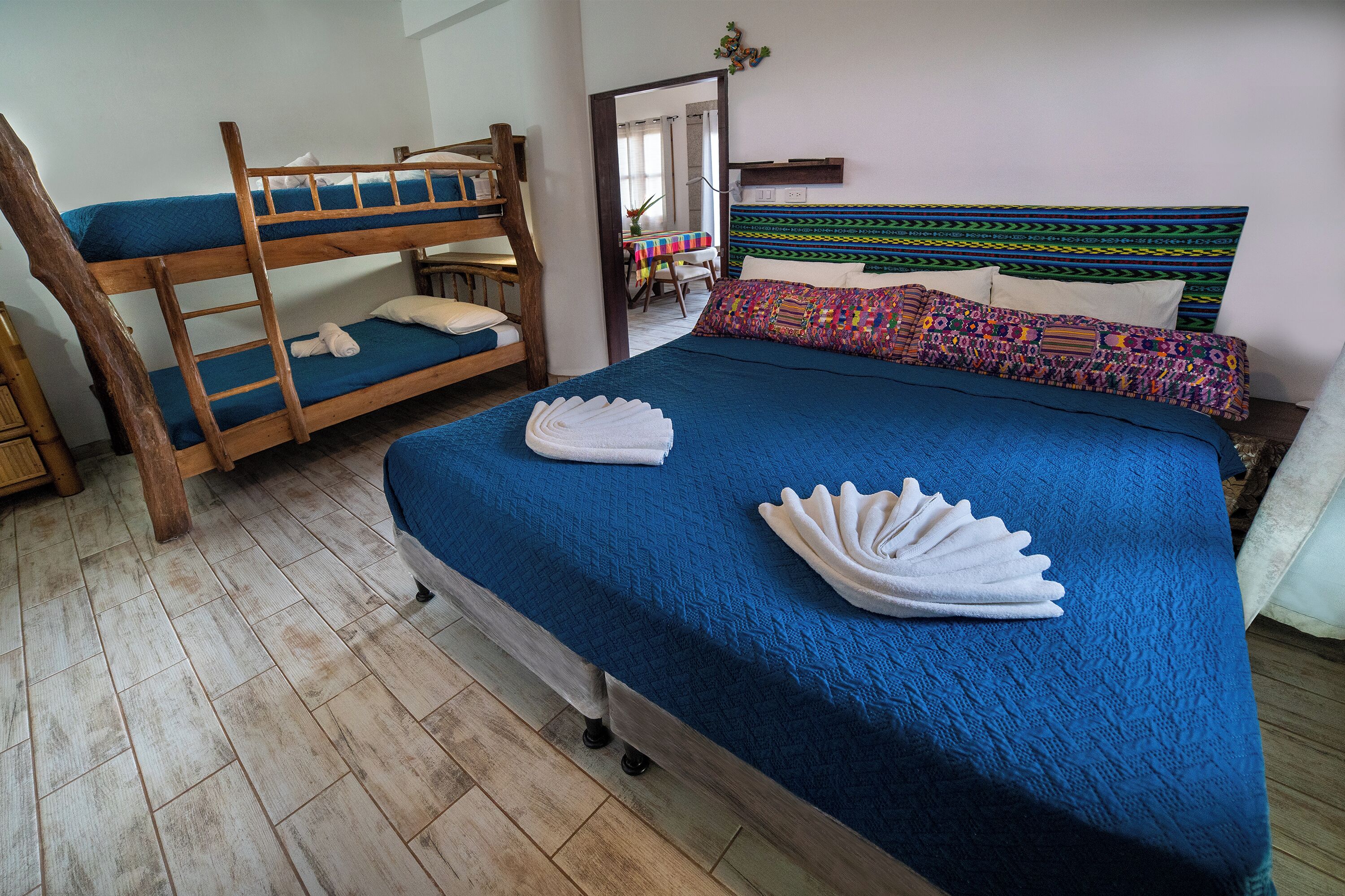Una habitación con literas, una cama grande con colcha azul y un cabecero colorido.