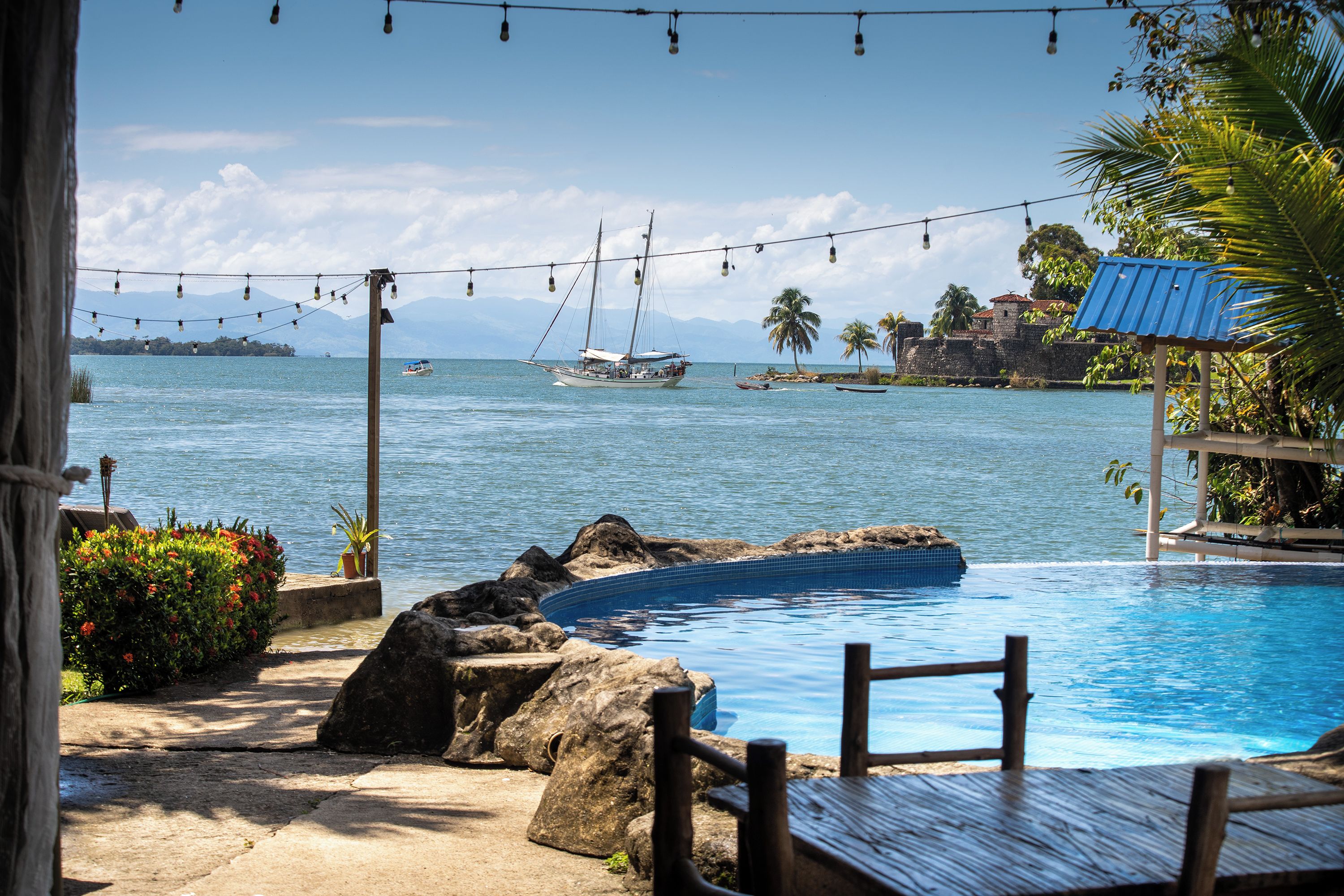 A pool area with a view of the sea, boats, and a distant island.