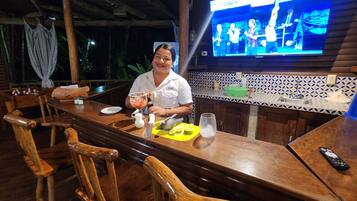 Zona de bar con muebles de madera, una pantalla de televisión y dispensador de agua.